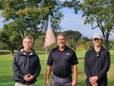 A trio of golfers prepare to tee-off with an American flag waving behind them