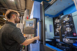 A man wearing safety glasses and working at a station with a keyboard and monitor.
