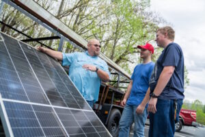 Three men standing next to a solar panel that has just been unloaded from a truck.