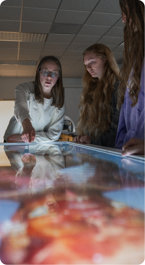 Students gathered around a table displaying an anatomical view of a human body