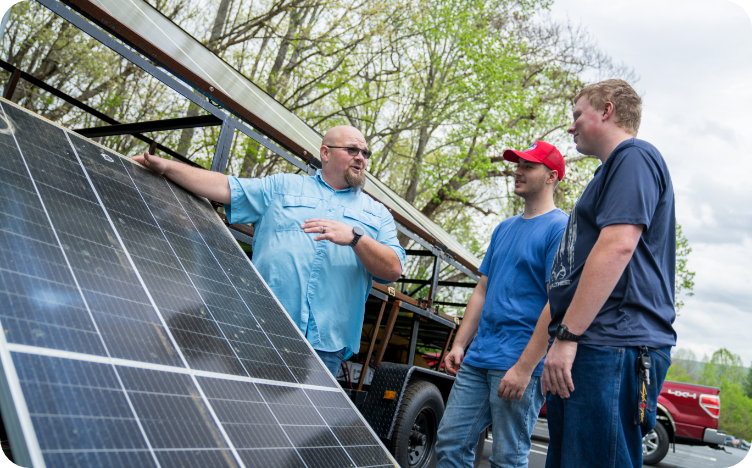 Three men standing next to a solar panel that has just been unloaded from a truck.