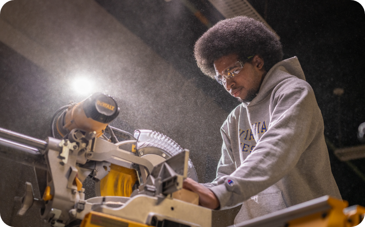 A man wearing a hoodie and safety glasses while working with a table saw.