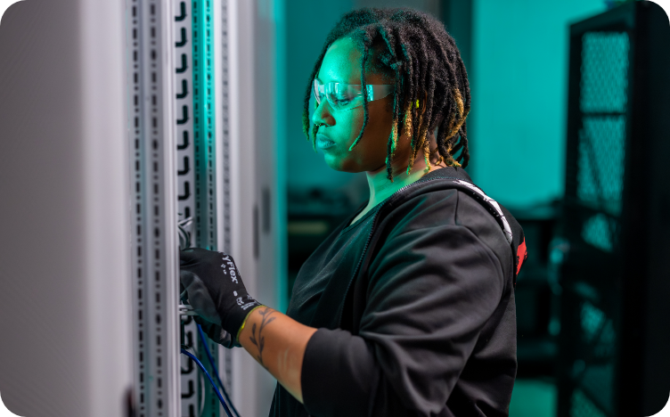 A woman wearing safety glasses and working at a server rack.