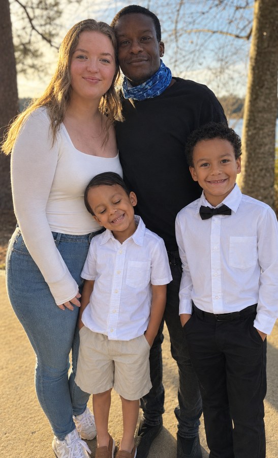 Malcolm and Skylar standing outdoors with their two sons, all dressed up for a family portrait