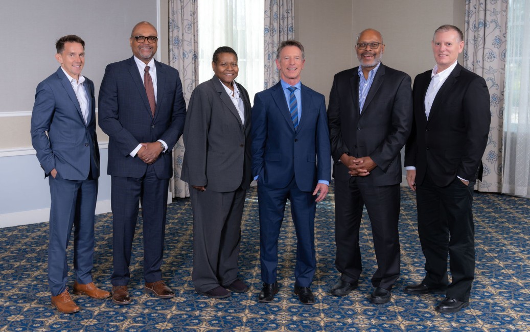 Six members of the VCCS Executive Cabinet standing together in business attire in a hotel meeting room.